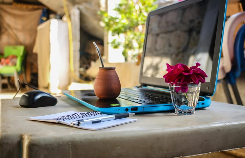 Espace de travail extérieur de digital nomad avec ordinateur portable, carnet de notes, café et des fleurs sur un bureau