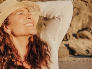 Femme digital nomad joyeuse avec un chapeau se prélasse au soleil au bord de la mer, symbole de liberté et de bonheur.